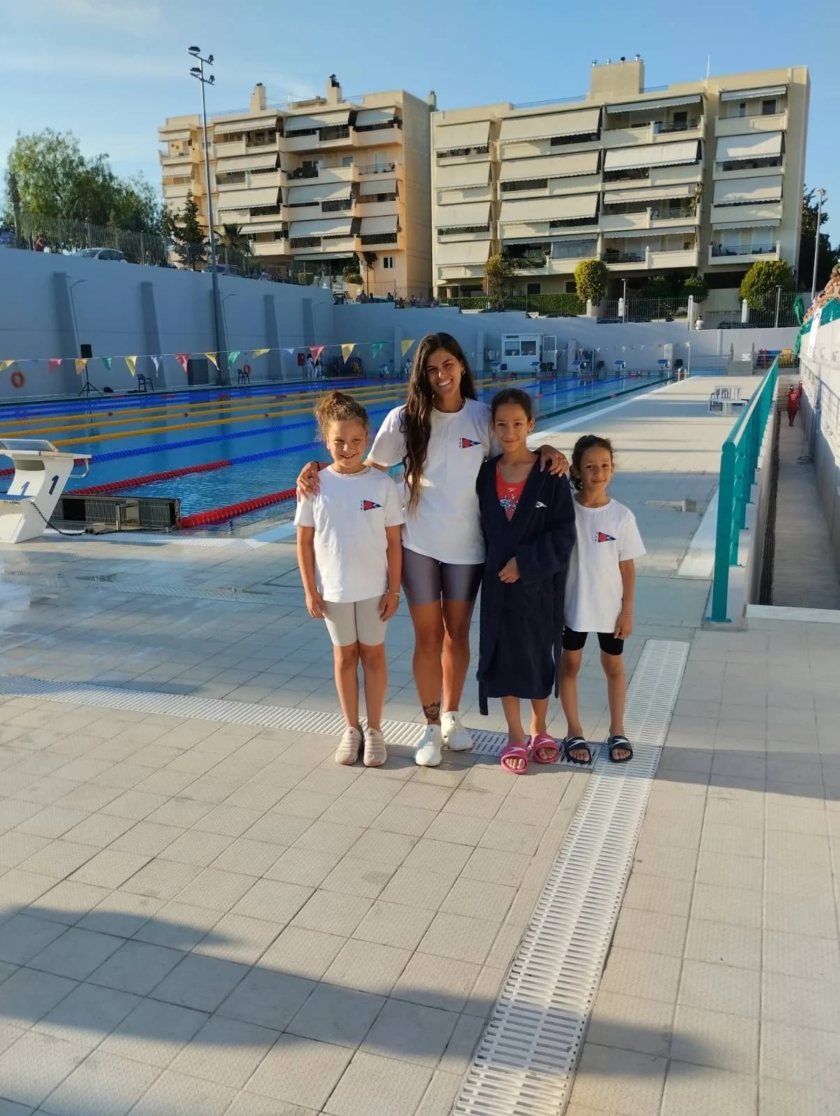 Προπονήτρια ποζάρει με τρία παιδιά της ομάδας δίπλα στην πισίνα